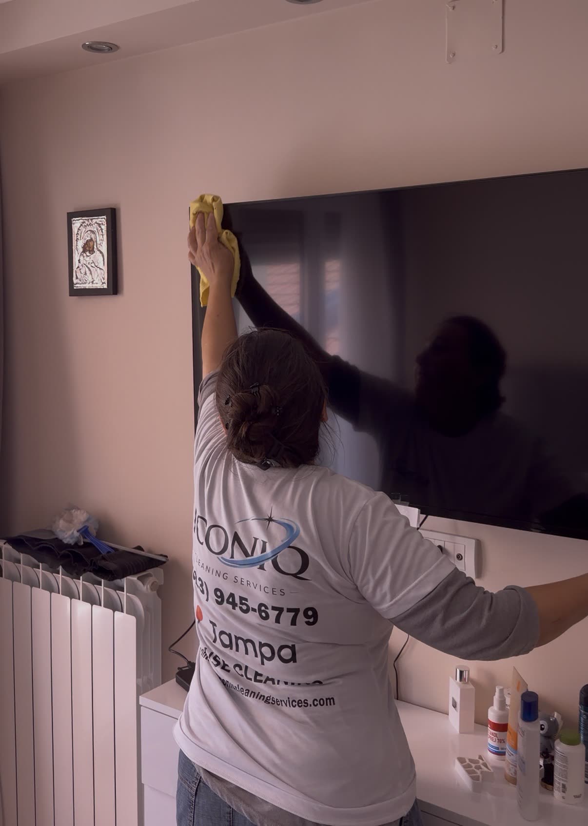 Iconiq cleaner dusting a TV and console in a Tampa living room